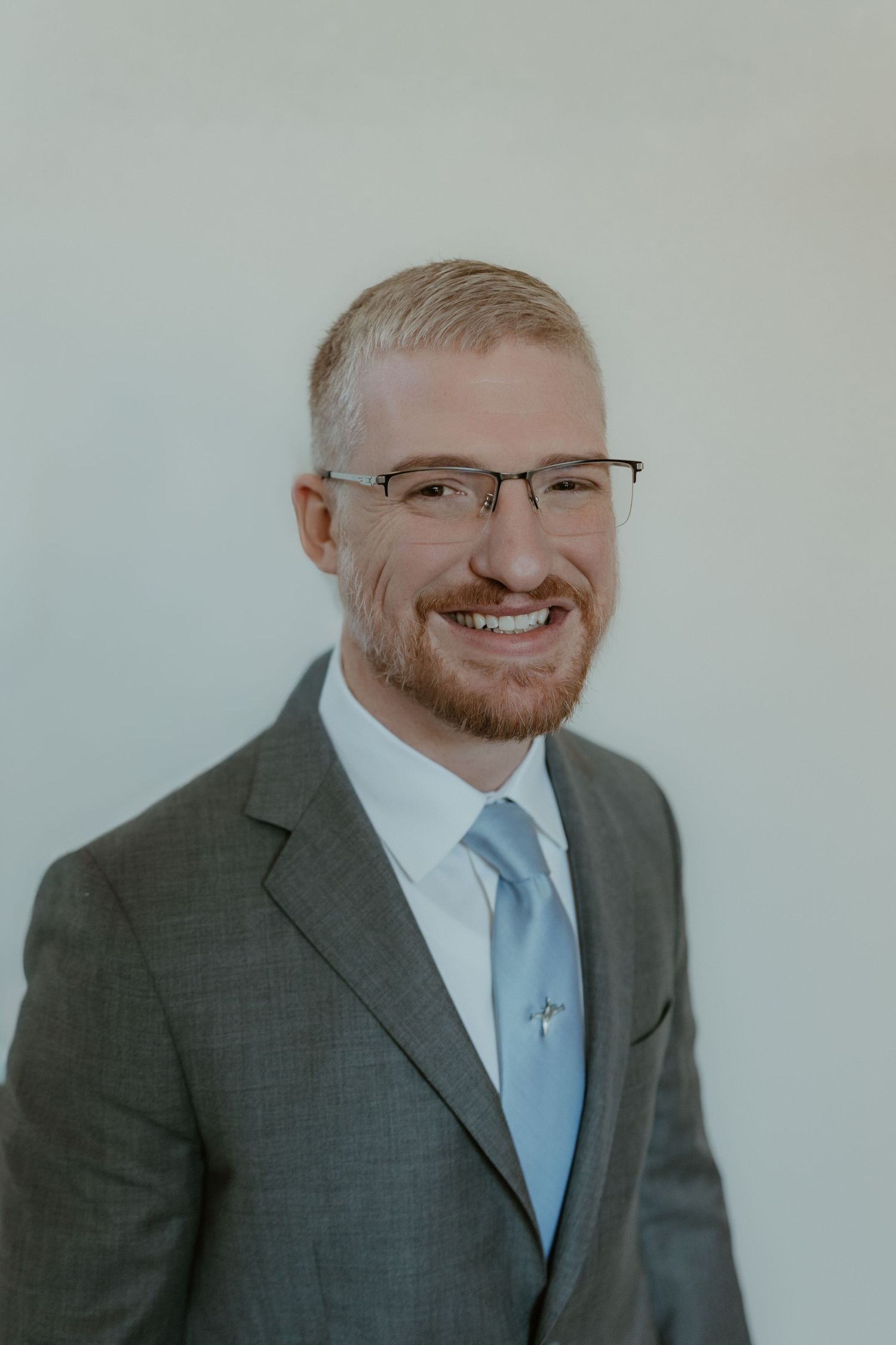 Professional headshot series showing different expressions while wearing a gray suit and light blue tie.