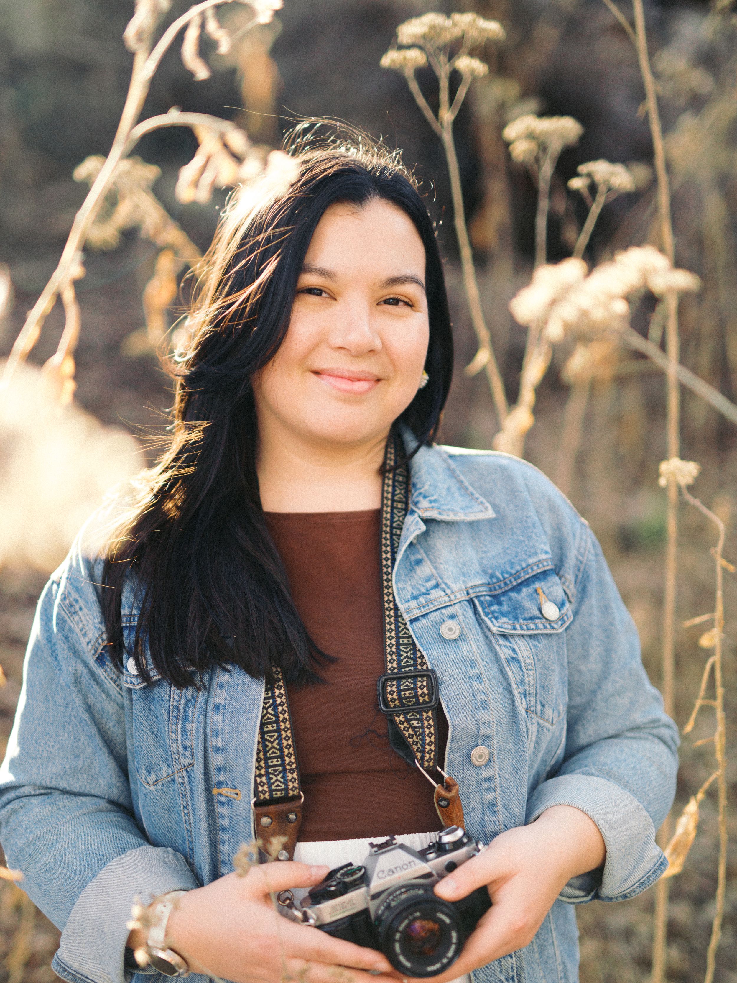 Rebecca Zamora Tristan, a Texas wedding and engagement photographer posing with her cameras in New Braunfels, Texas