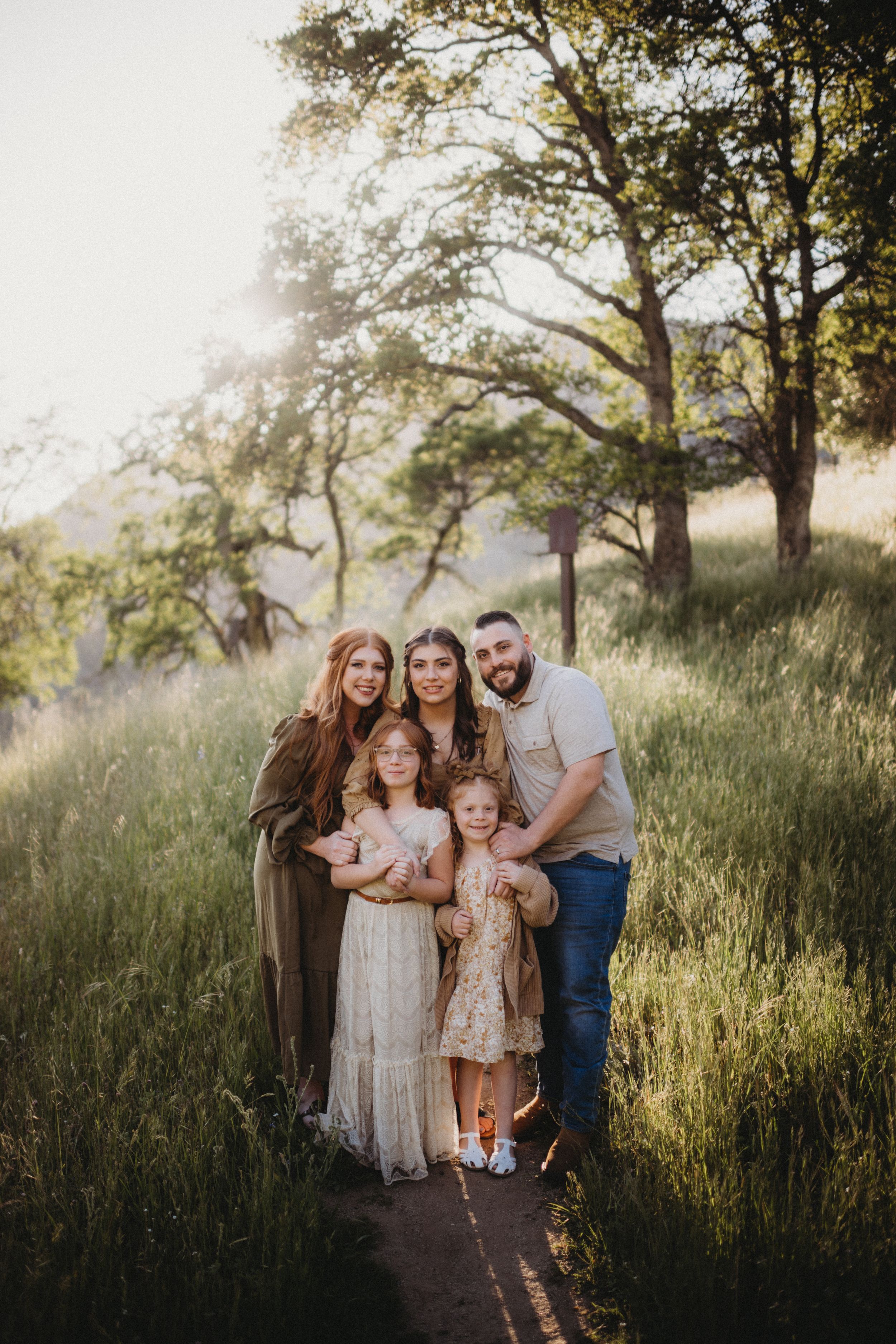 A family portrait in golden evening light on a hillside trail surrounded by tall grass.