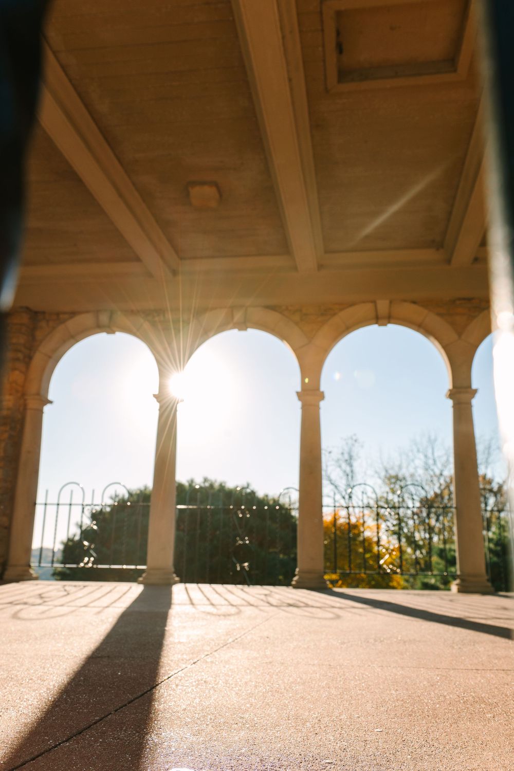 Sunlit stone archway with classical columns casting dramatic shadows on a terrace.
