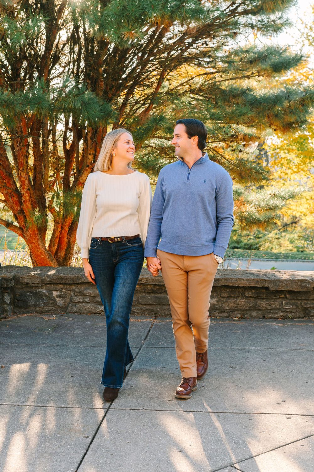 Couple walking together on a stone path surrounded by trees during a sunny afternoon.