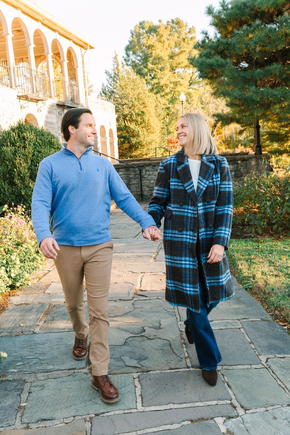 Couple walking together on stone pavement during autumn wearing blue and plaid outfits.