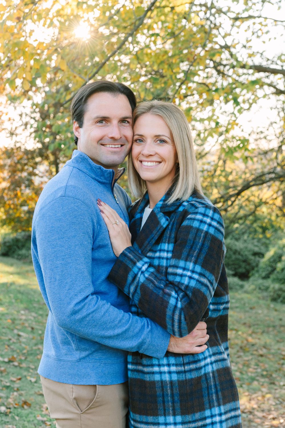 A romantic autumn portrait of a couple embracing outdoors in coordinating blue outfits against fall foliage.