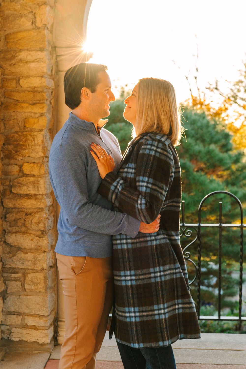 A couple sharing an intimate moment at sunset against a stone archway while wearing coordinated casual attire.