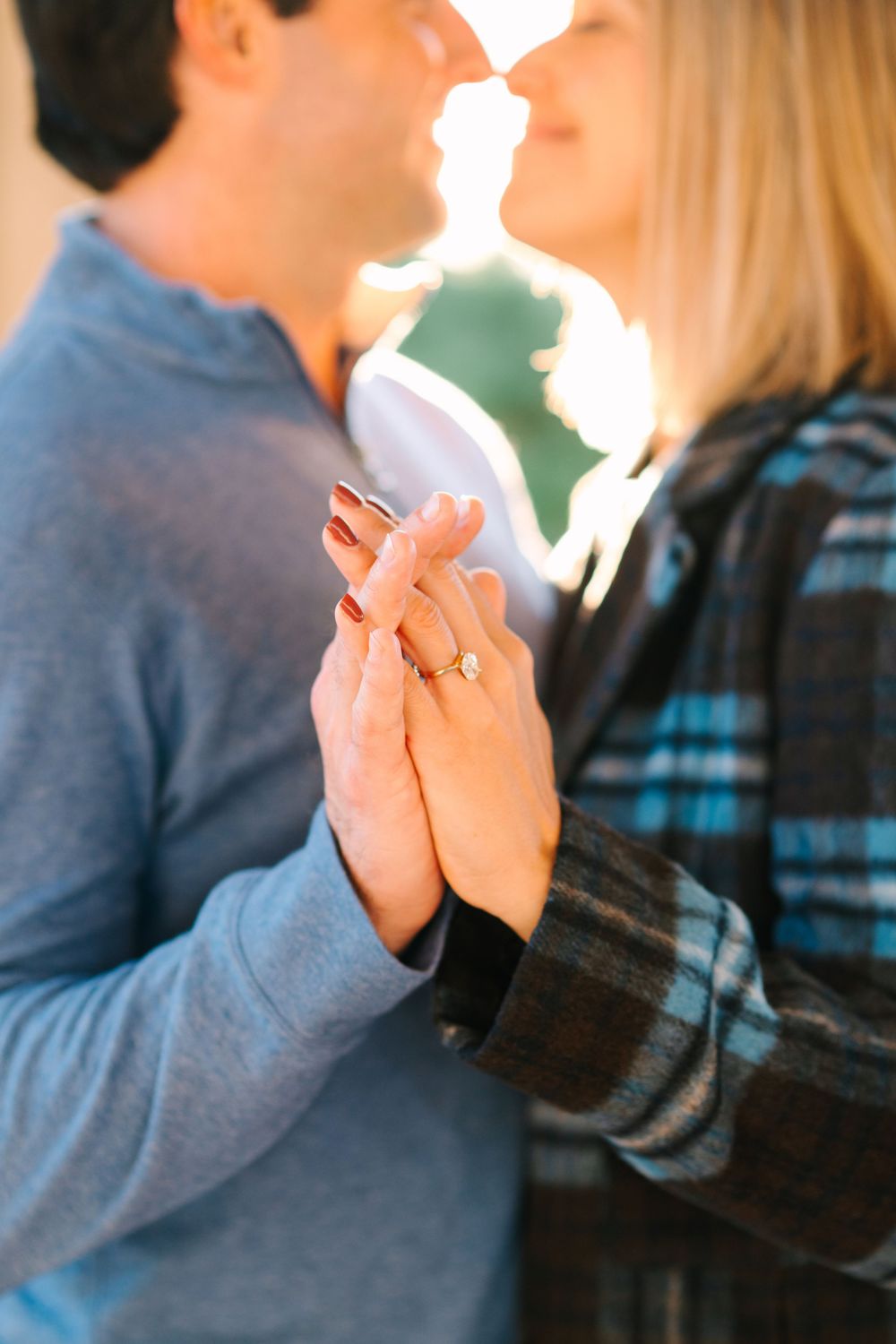 Close-up shot of clasped hands with an engagement ring glinting in golden sunlight.