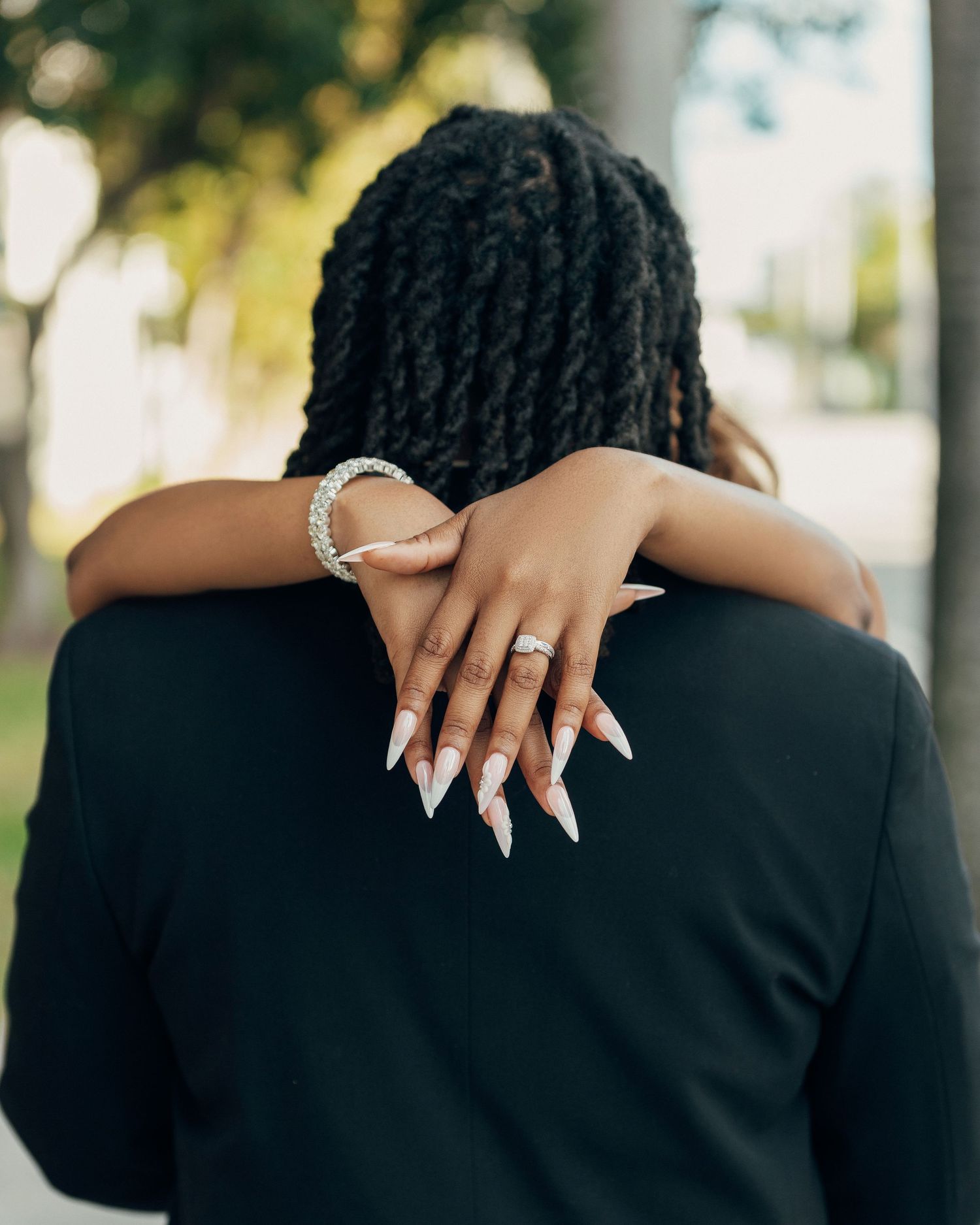 Long acrylic nails and jewelry displayed as arms embrace during an intimate moment.
