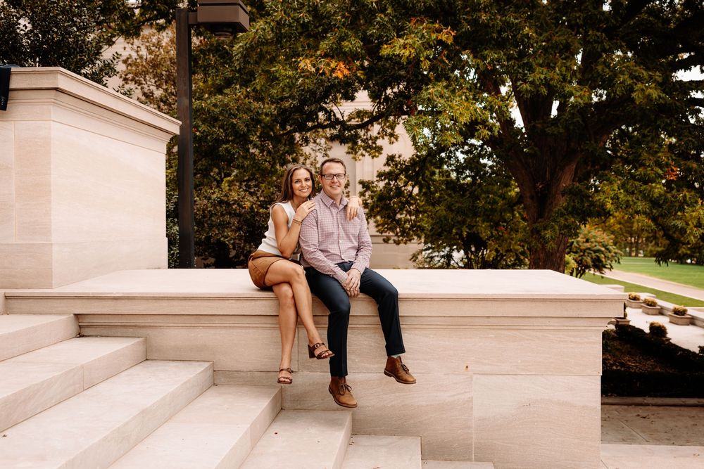 A couple sits together on outdoor stone steps during a romantic engagement photo session at National Galleria in Washington DC