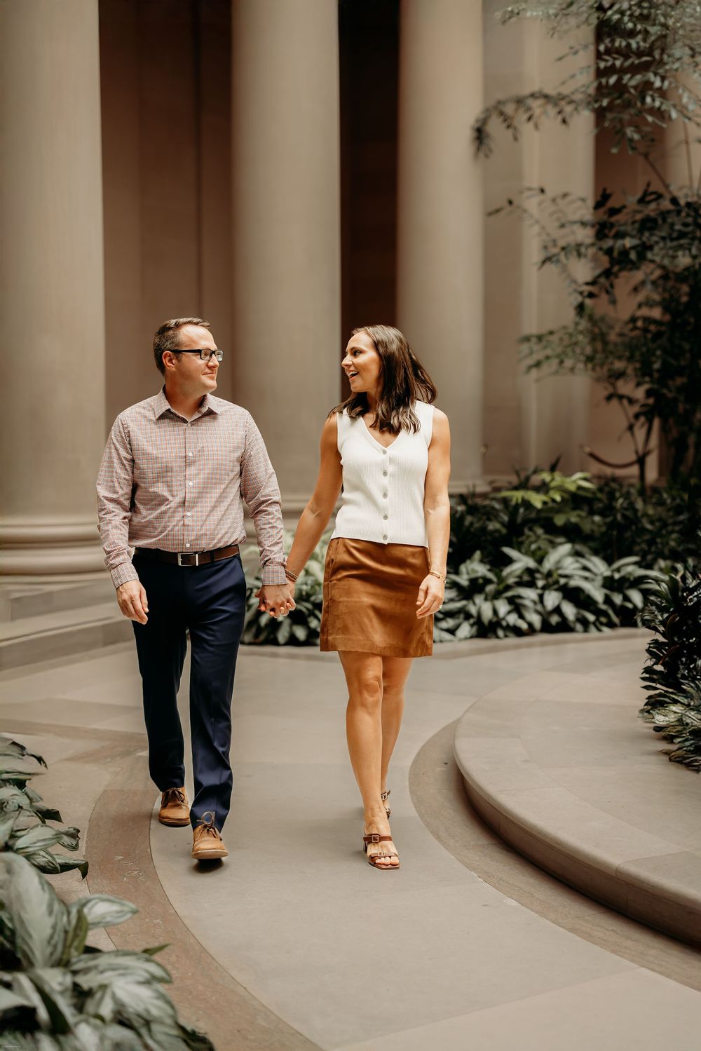 A couple walks together along a curved colonnade path during an engagement photo session at National Galleria in Washington DC
