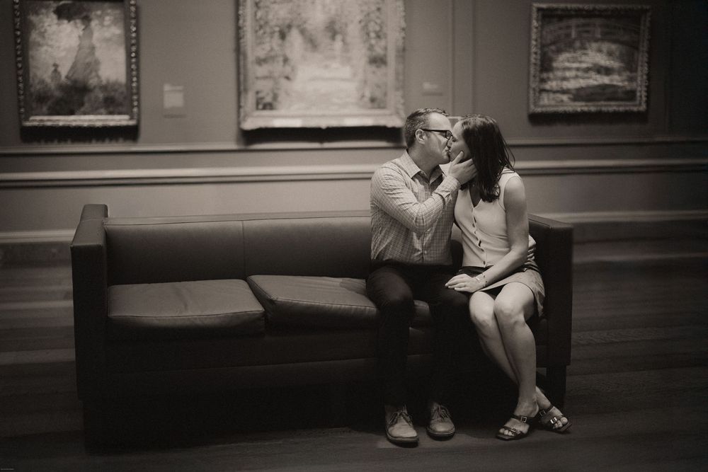 Couple have an intimate moment sitting on benches in an art gallery viewing paintings .DC Engagement at the National Galleria.