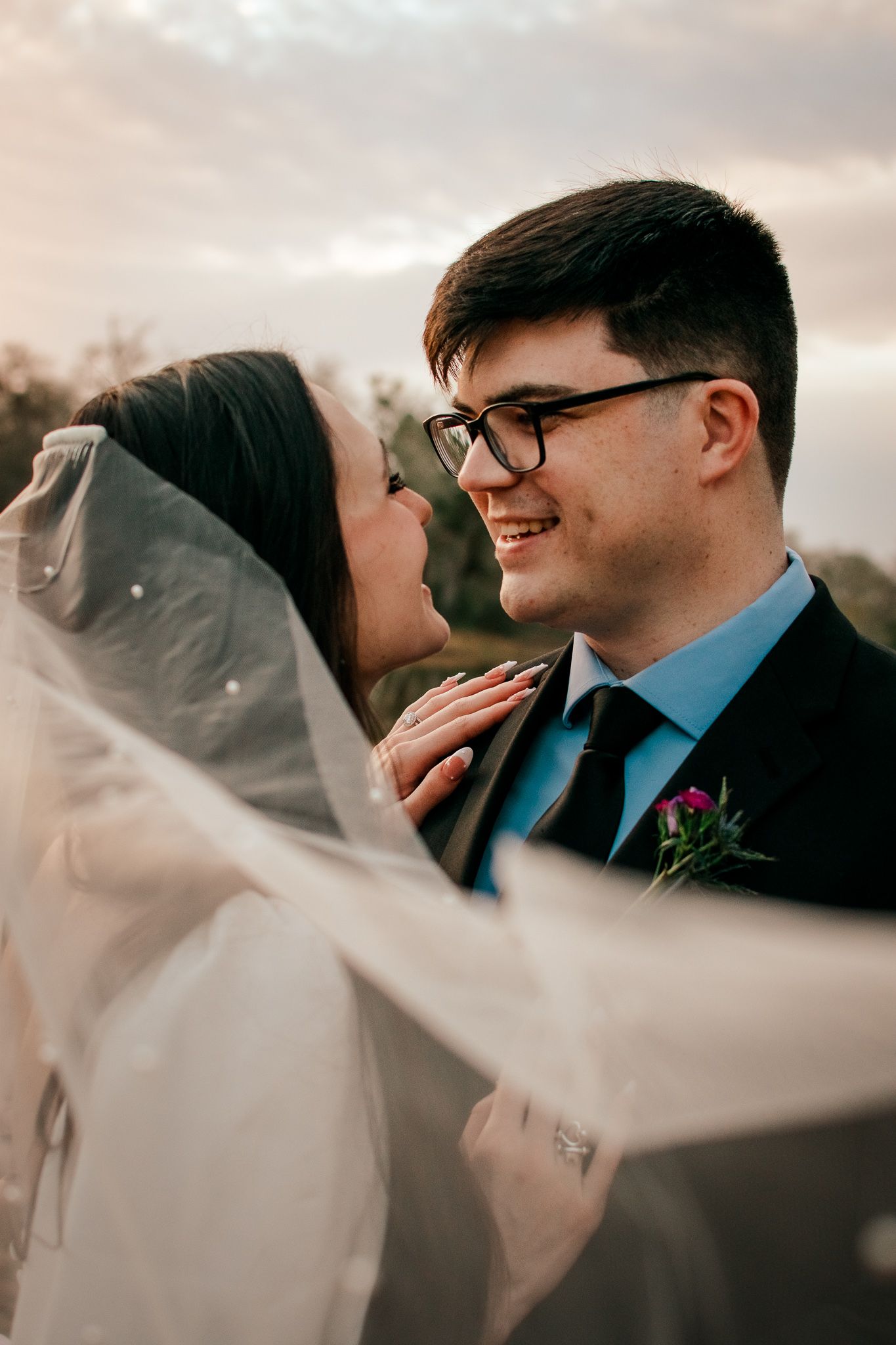 A joyful wedding moment captured at sunset with the bride's veil flowing in the breeze.
