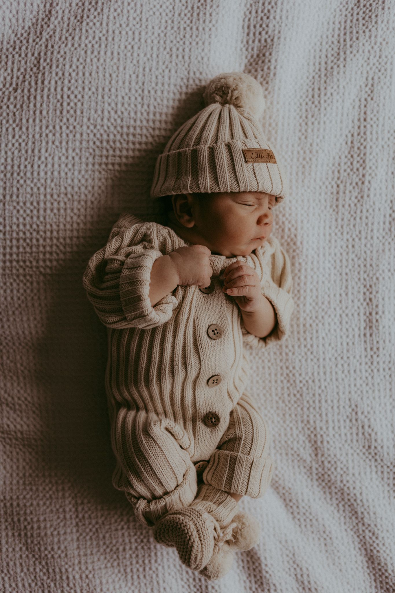 Sleeping newborn baby dressed in cream knit romper and pom pom beanie hat.