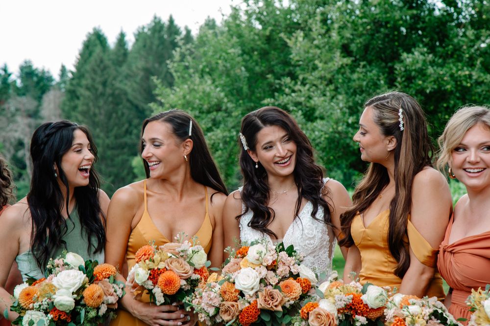 Hayloft in The Grove Wedding, bridesmaids in orange and yellow dresses hold peach and orange bouquets while smiling outdoors.