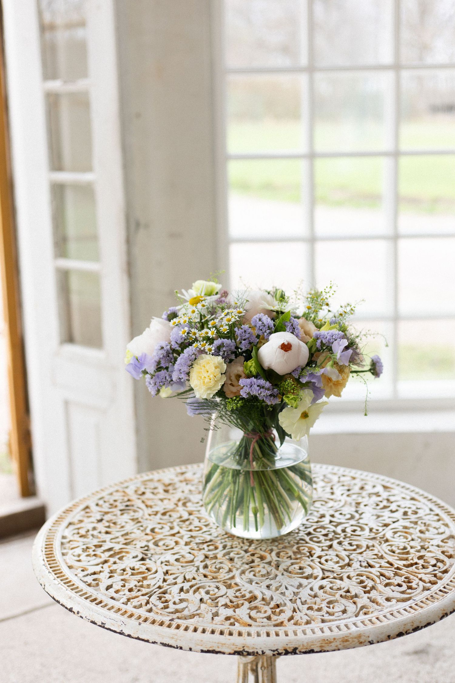 A delicate spring bouquet in soft purples and whites displayed on an ornate white table.