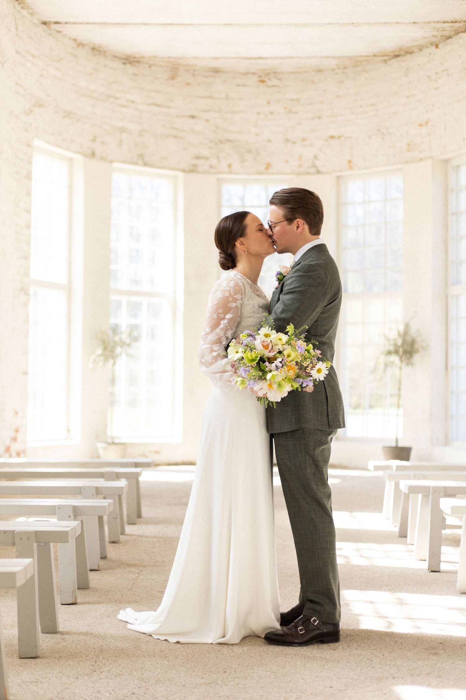 A romantic wedding ceremony in a sunlit chapel with wooden pews and a beautiful spring bouquet.