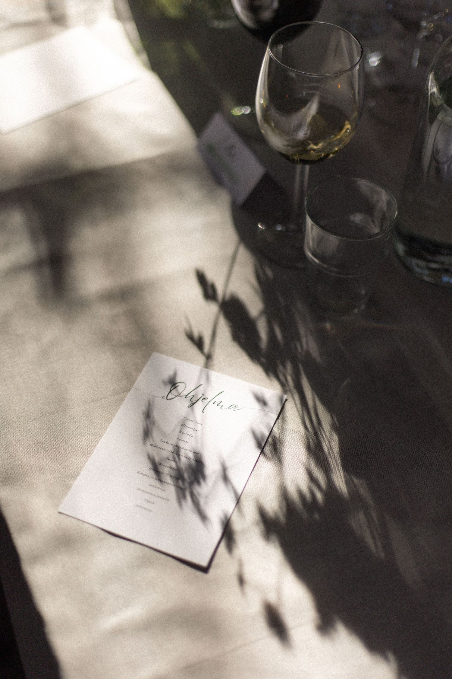 Artistic shadow play on wedding stationery with wine glass in soft natural light.