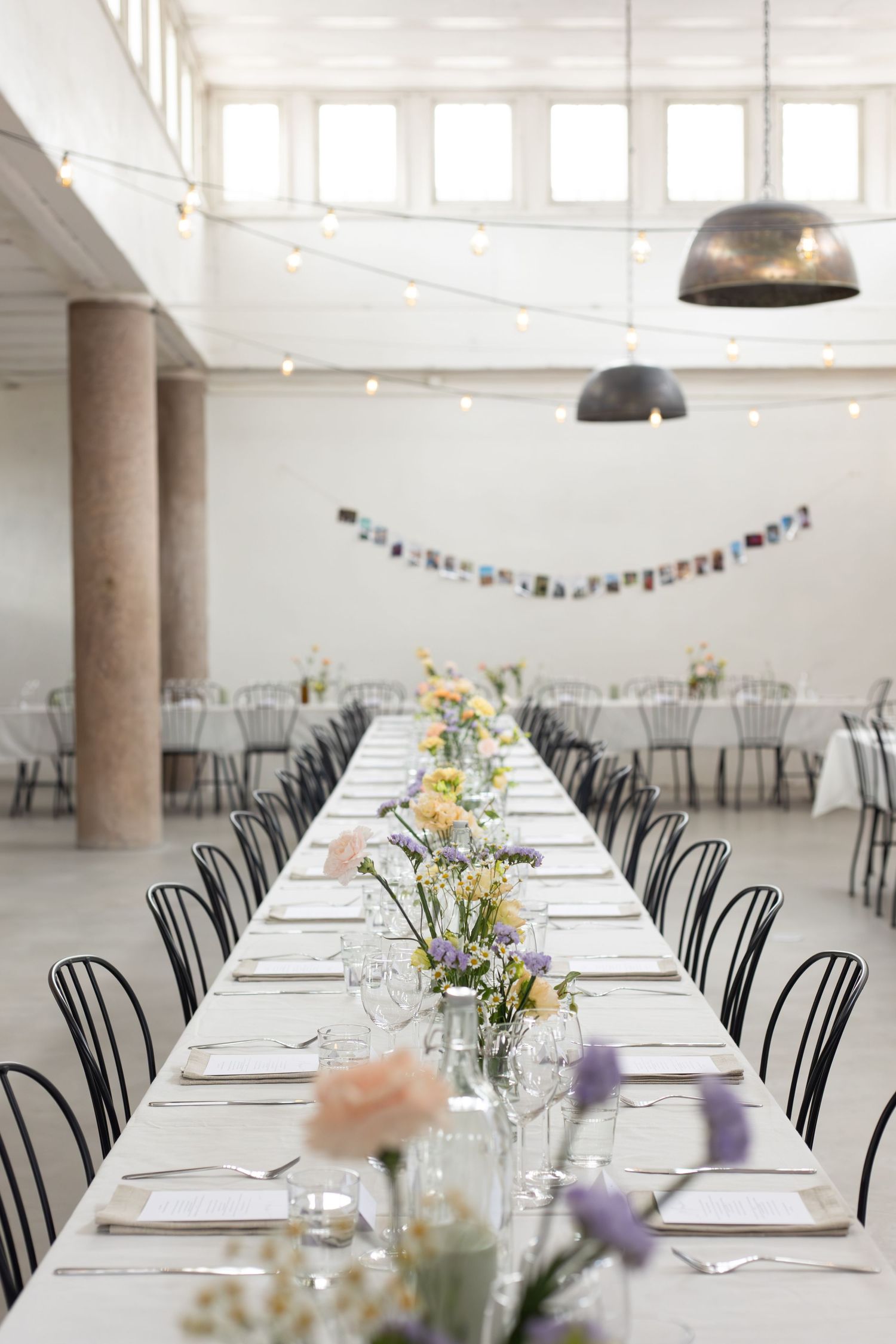 Minimalist wedding reception venue with long tables, black chairs and industrial pendant lights.