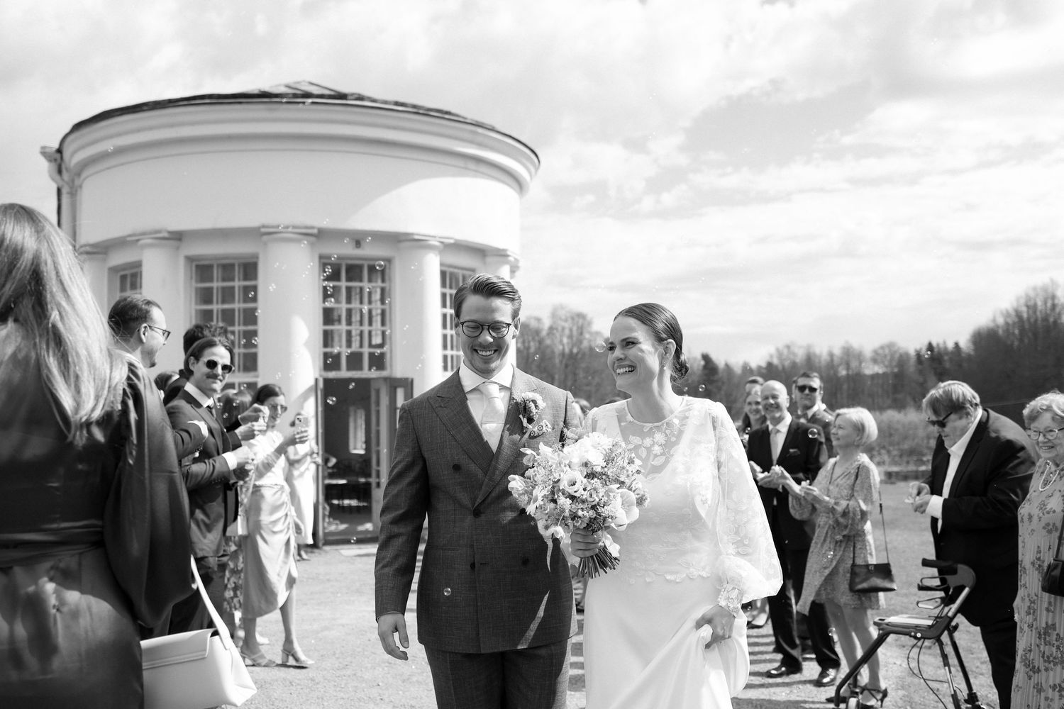A joyful wedding ceremony exit at a white columned venue with guests celebrating.
