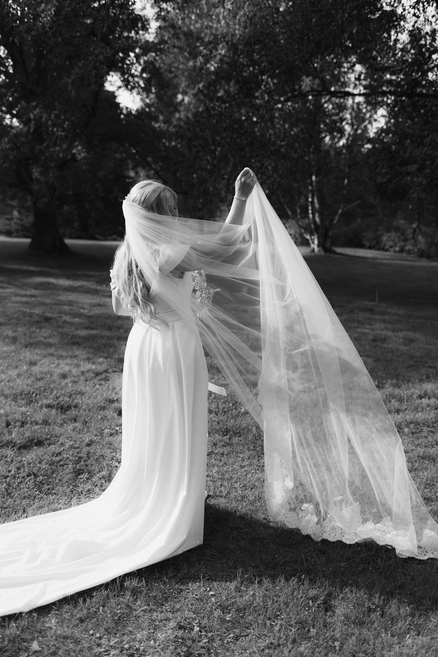 Black and white photo of a flowing wedding dress and veil in a garden setting.