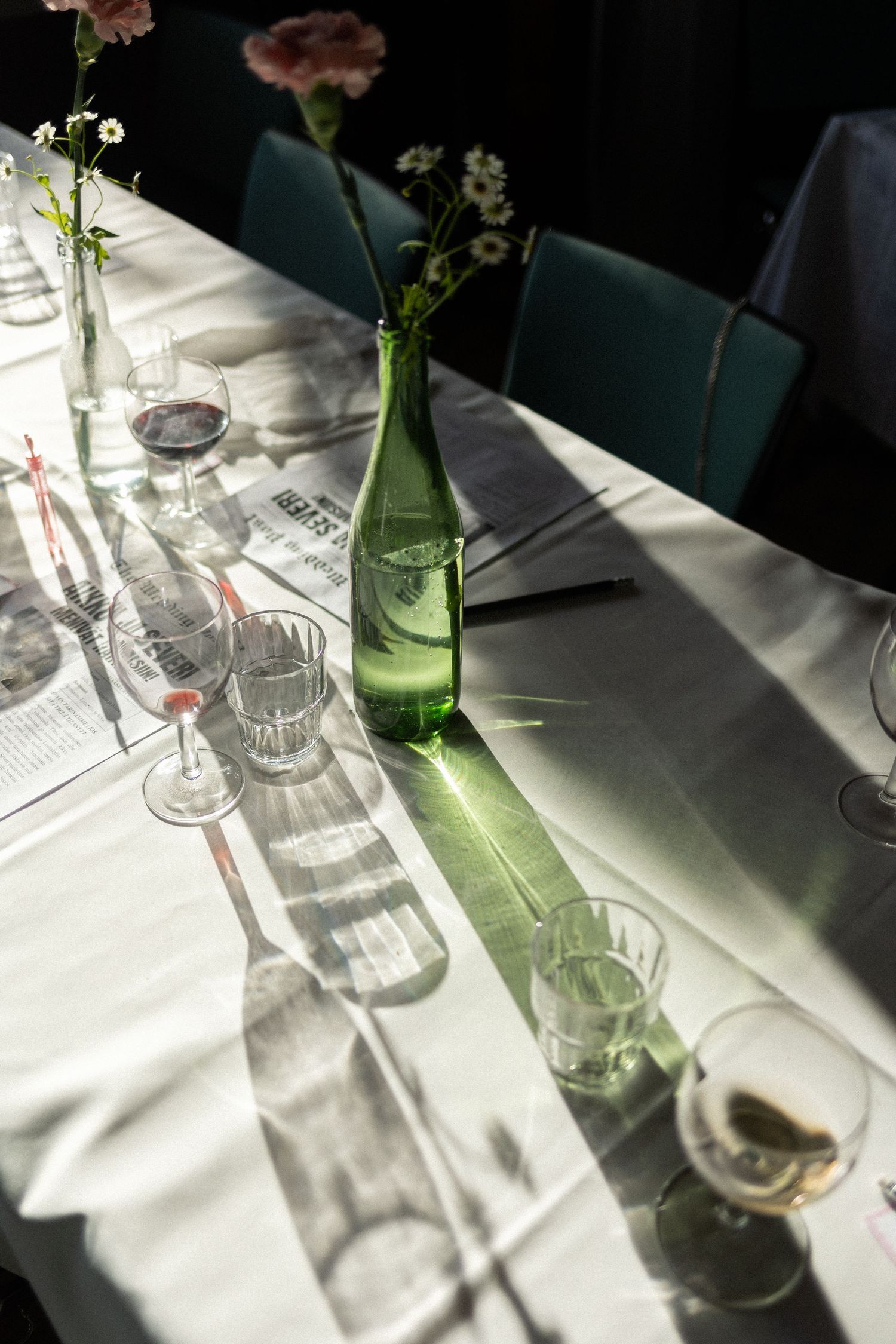 Elegant table setting with green glass bottle vase casting dramatic shadows on white tablecloth.