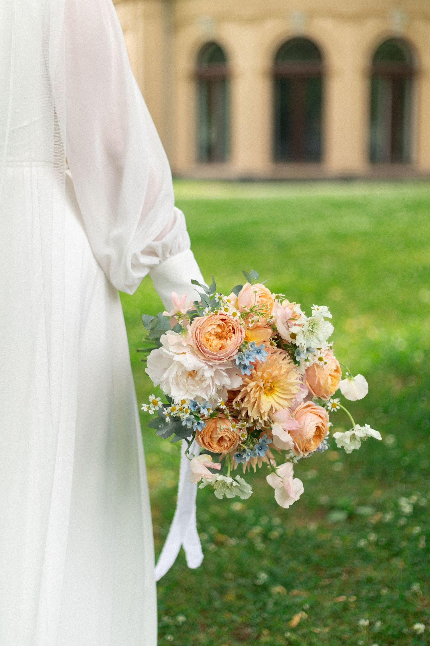 Peach and cream wedding bouquet with garden roses held against a white dress.
