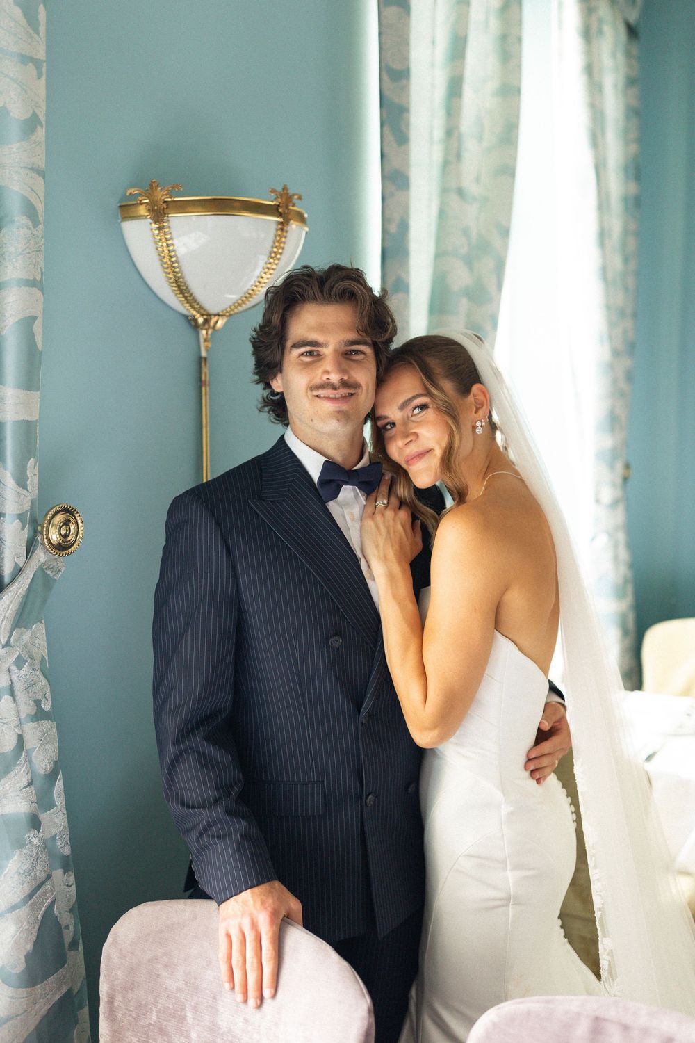 A bride and groom share intimate moments in a turquoise-walled room with elegant decor and flowing curtains.