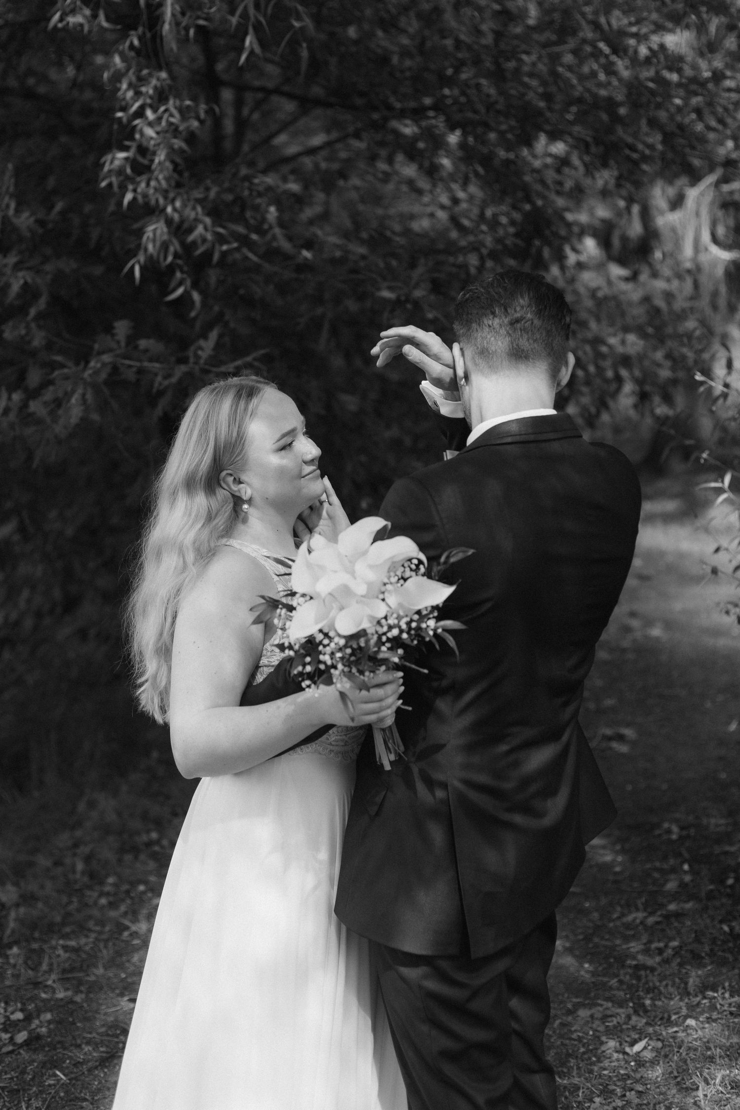 Black and white portrait of a couple sharing a joyful moment outdoors with bouquet.