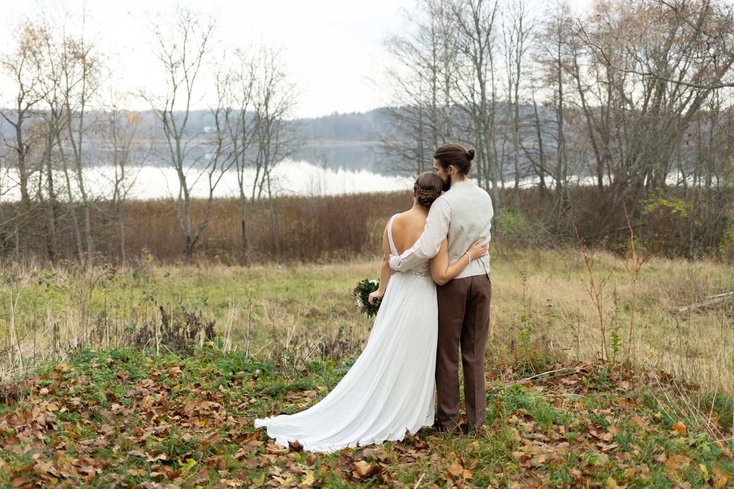 A couple in wedding attire overlooking a scenic lake view in autumn.