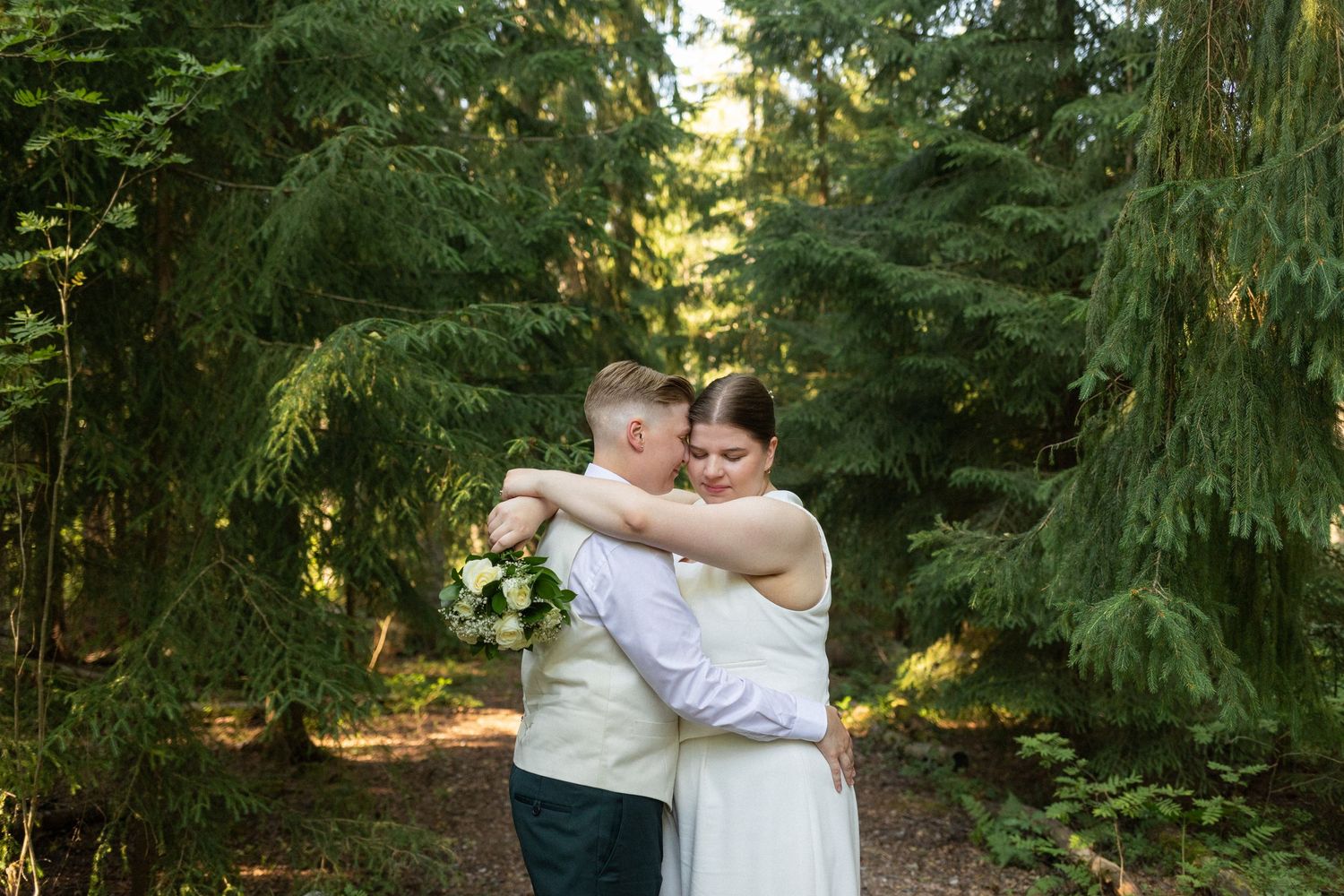 Newlyweds embrace in a serene forest setting surrounded by evergreen trees.