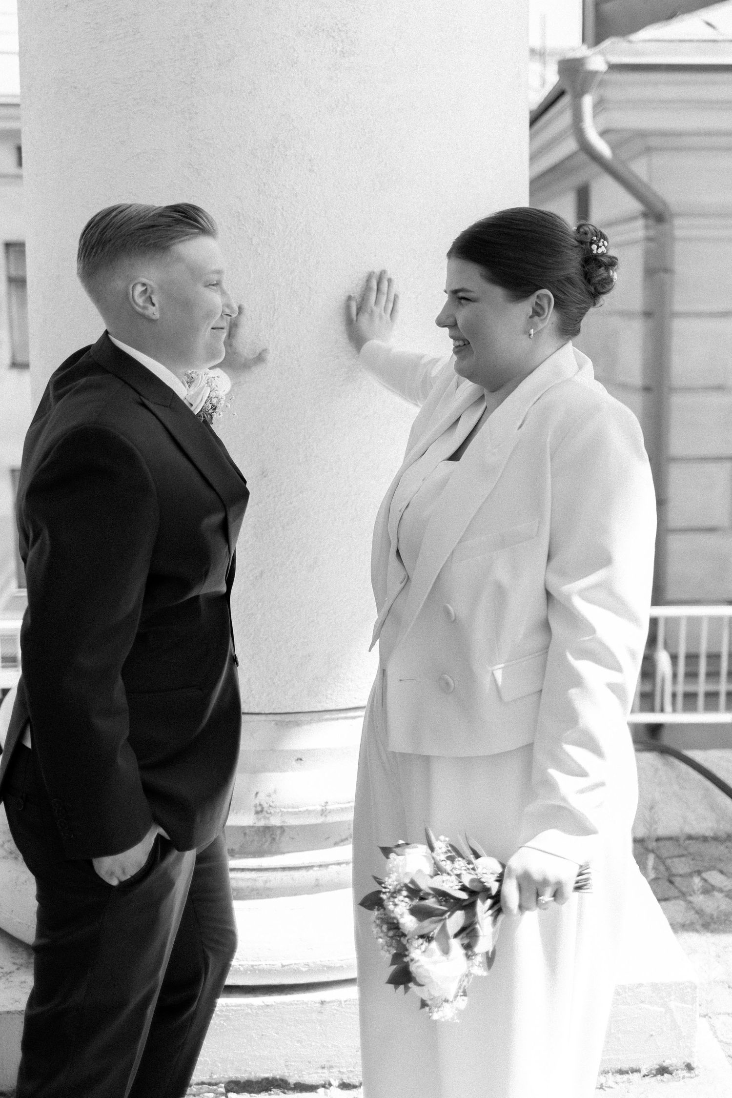Wedding couple in formal attire sharing an intimate moment beside a grand white column.