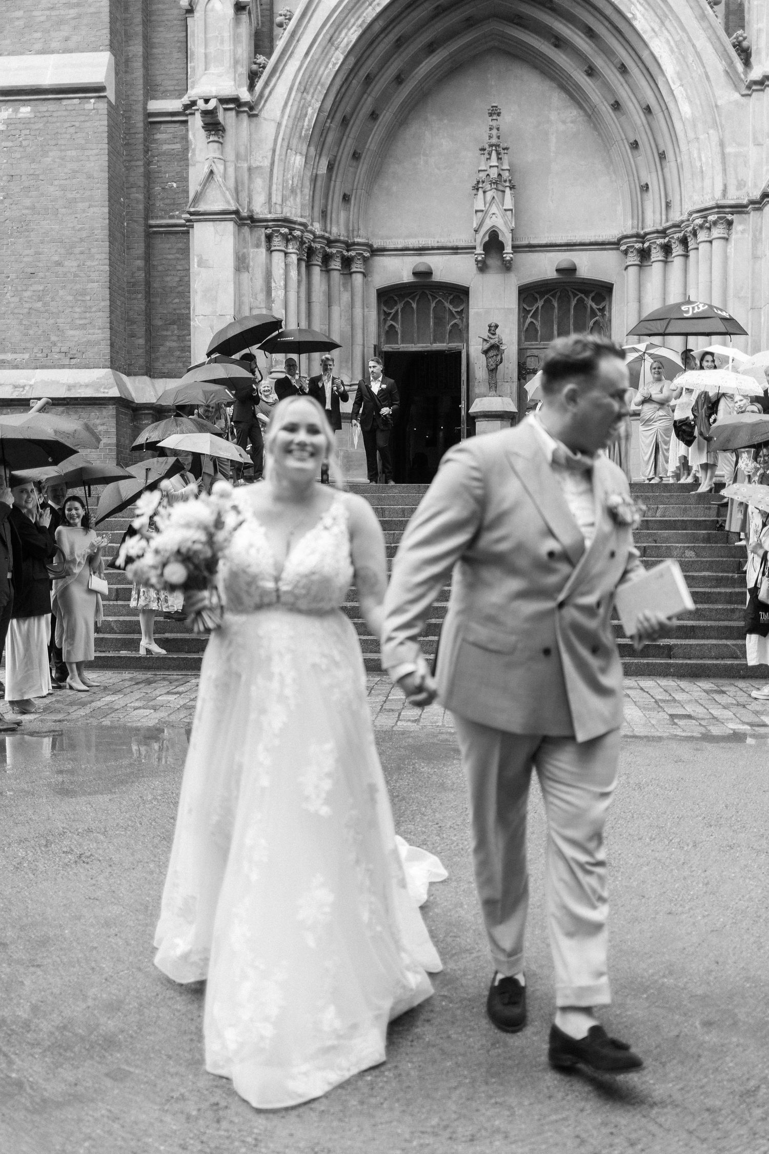 A rainy wedding day scene outside a historic church with umbrellas.