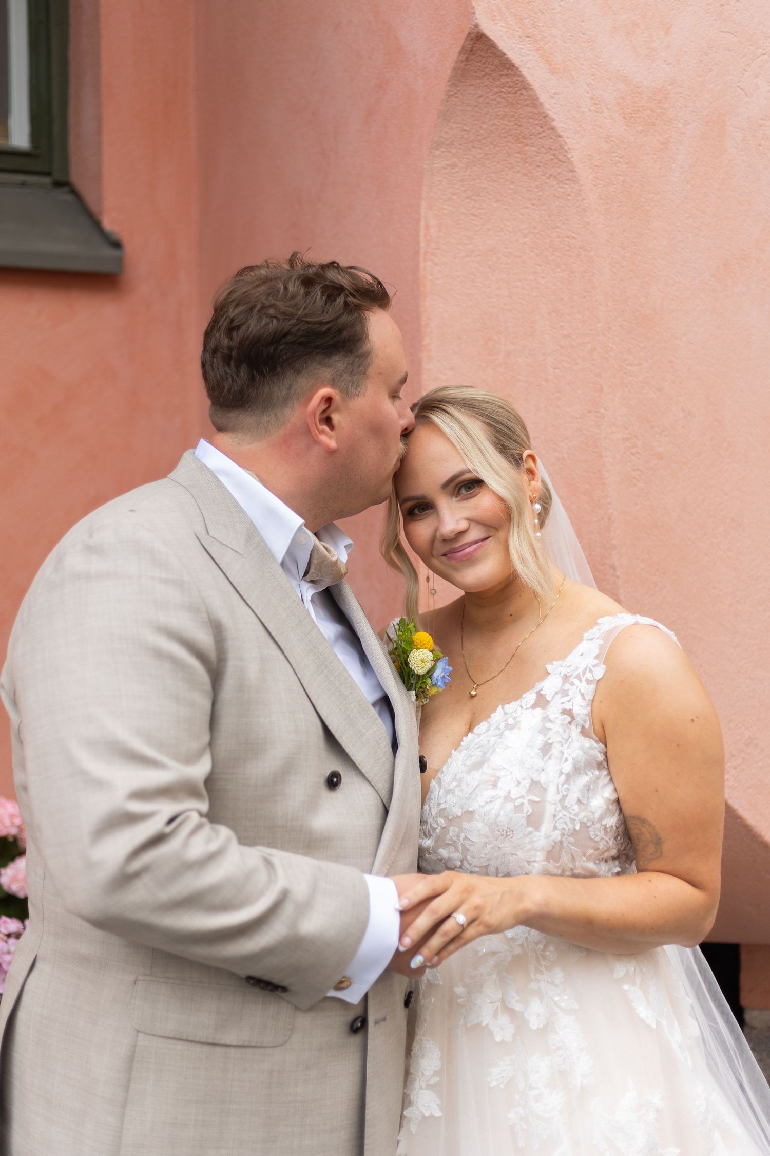 Romantic moment captured against coral colored wall during wedding photoshoot.
