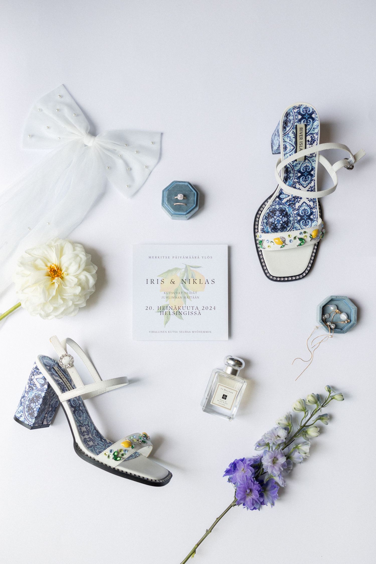 Wedding flat lay with blue floral sandals, white bow, perfume bottle and delicate flowers on light background.