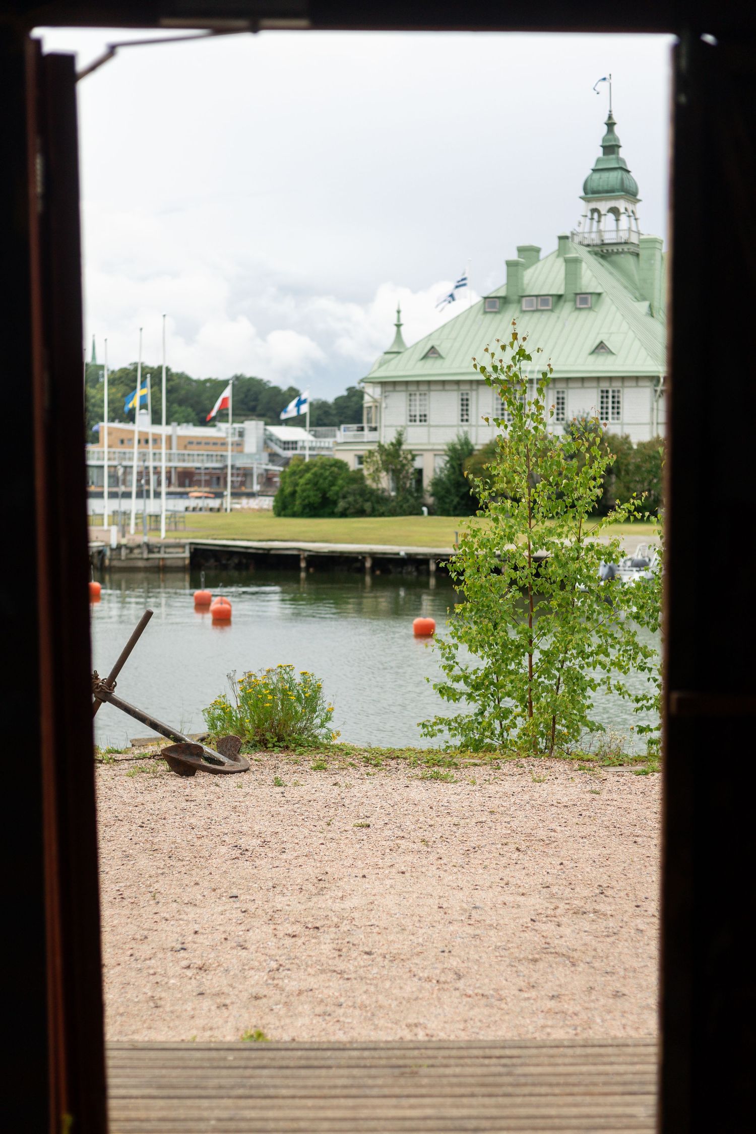 View of a historic green-roofed building with a spire near a waterfront through a window frame.