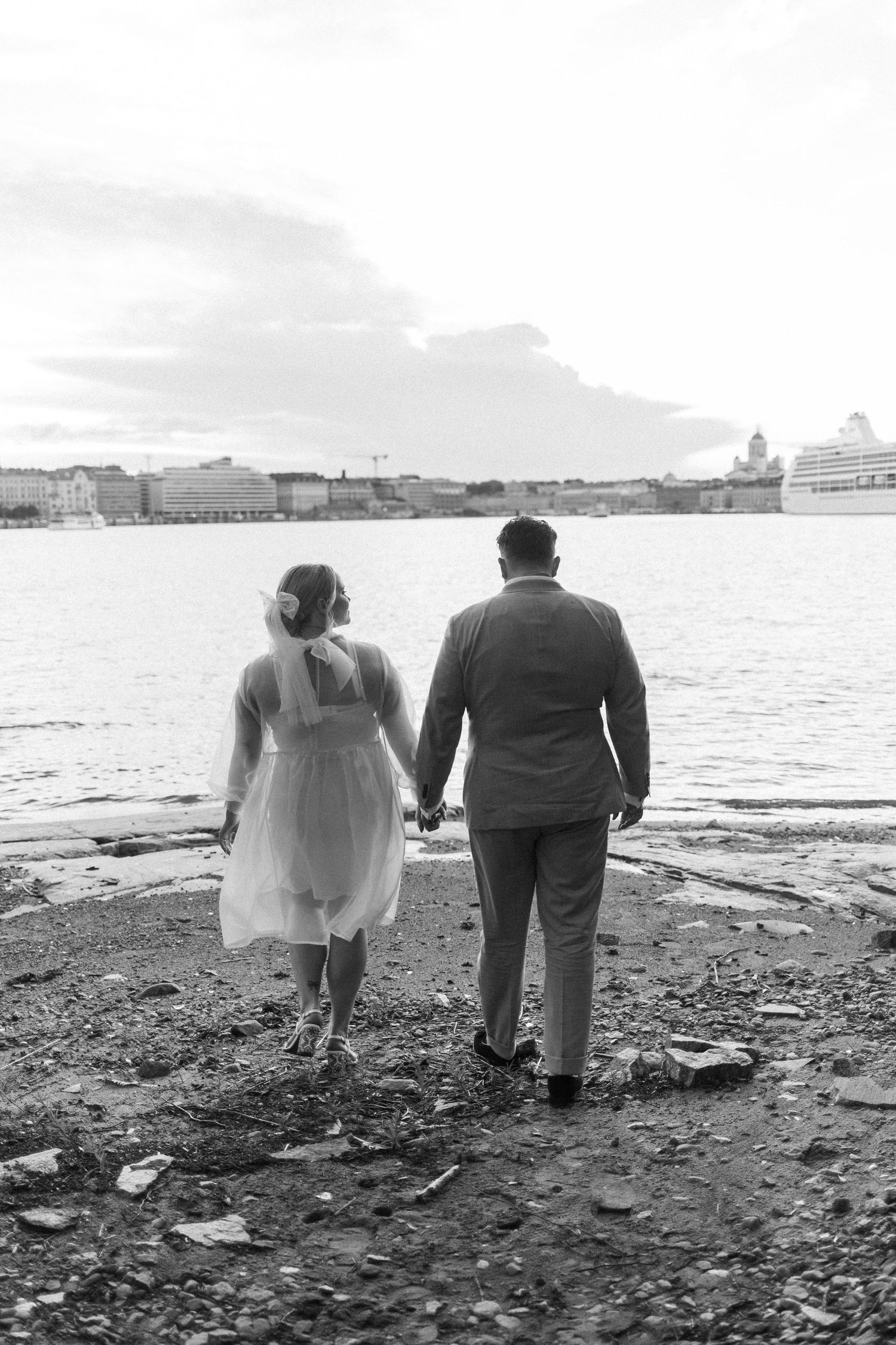 Black and white photo of a couple standing by the waterfront with cruise ships in the distance.