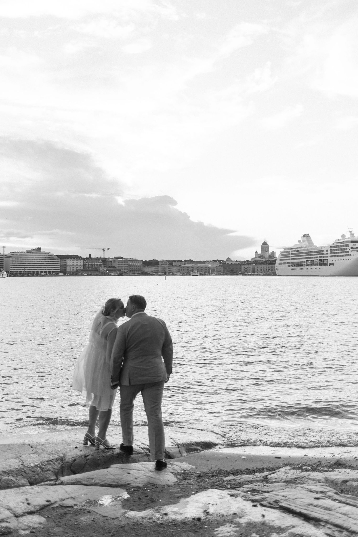 A romantic waterfront moment with ships and harbor buildings visible in the background.
