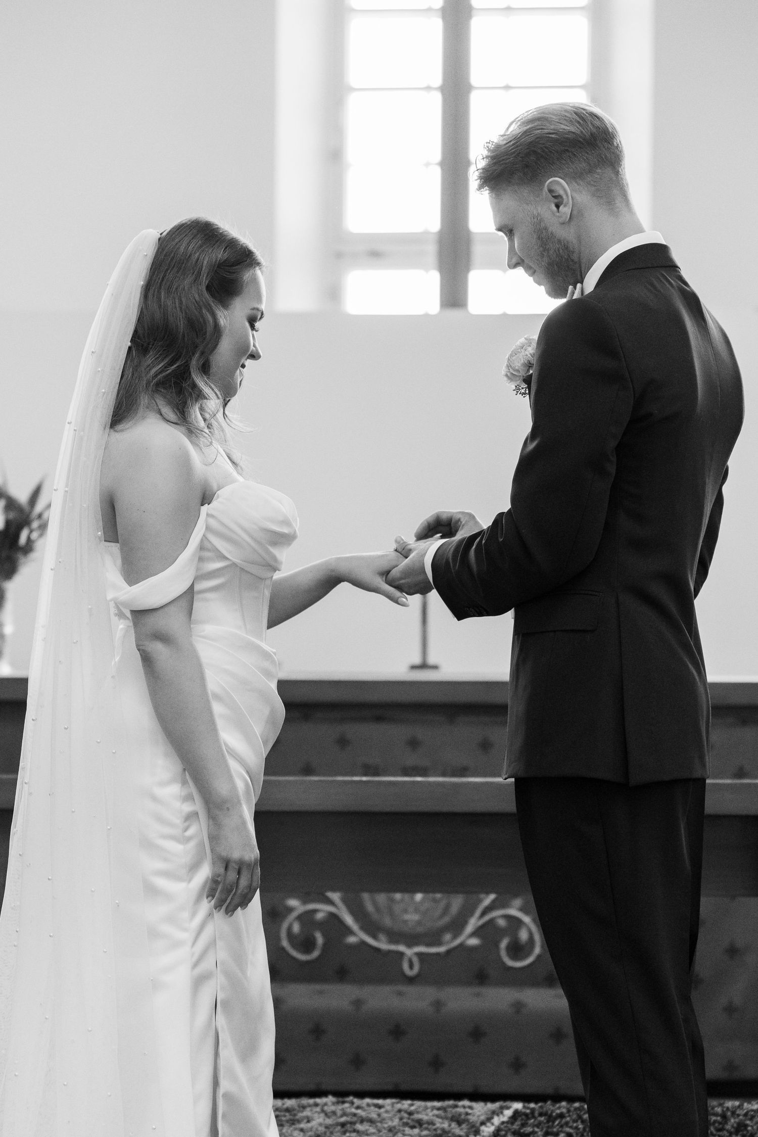 Intimate black and white photo of a couple exchanging rings during wedding ceremony.