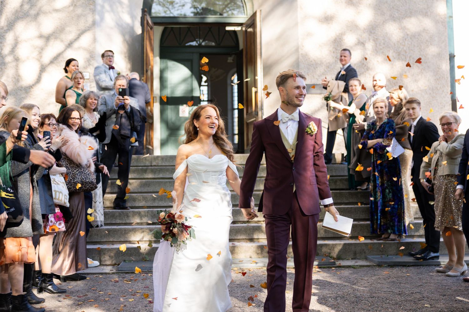 Newlyweds exit church while guests shower them with confetti on sunny wedding day.