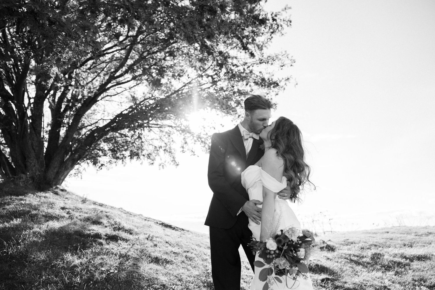 A romantic black and white wedding photo with sunlight streaming through trees.