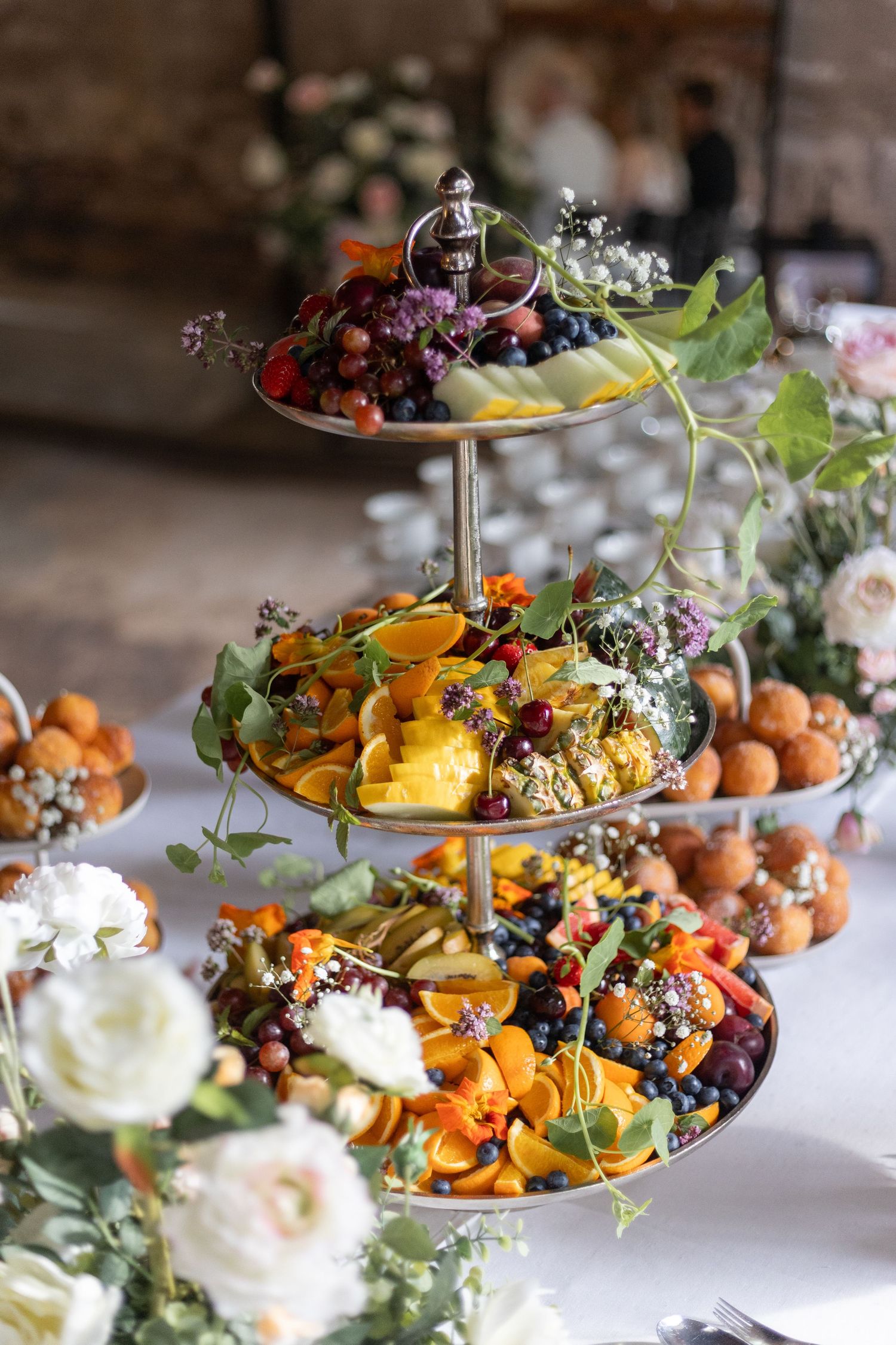 Elegant tiered dessert platter with fresh fruits, flowers and appetizers arranged beautifully for a celebration.