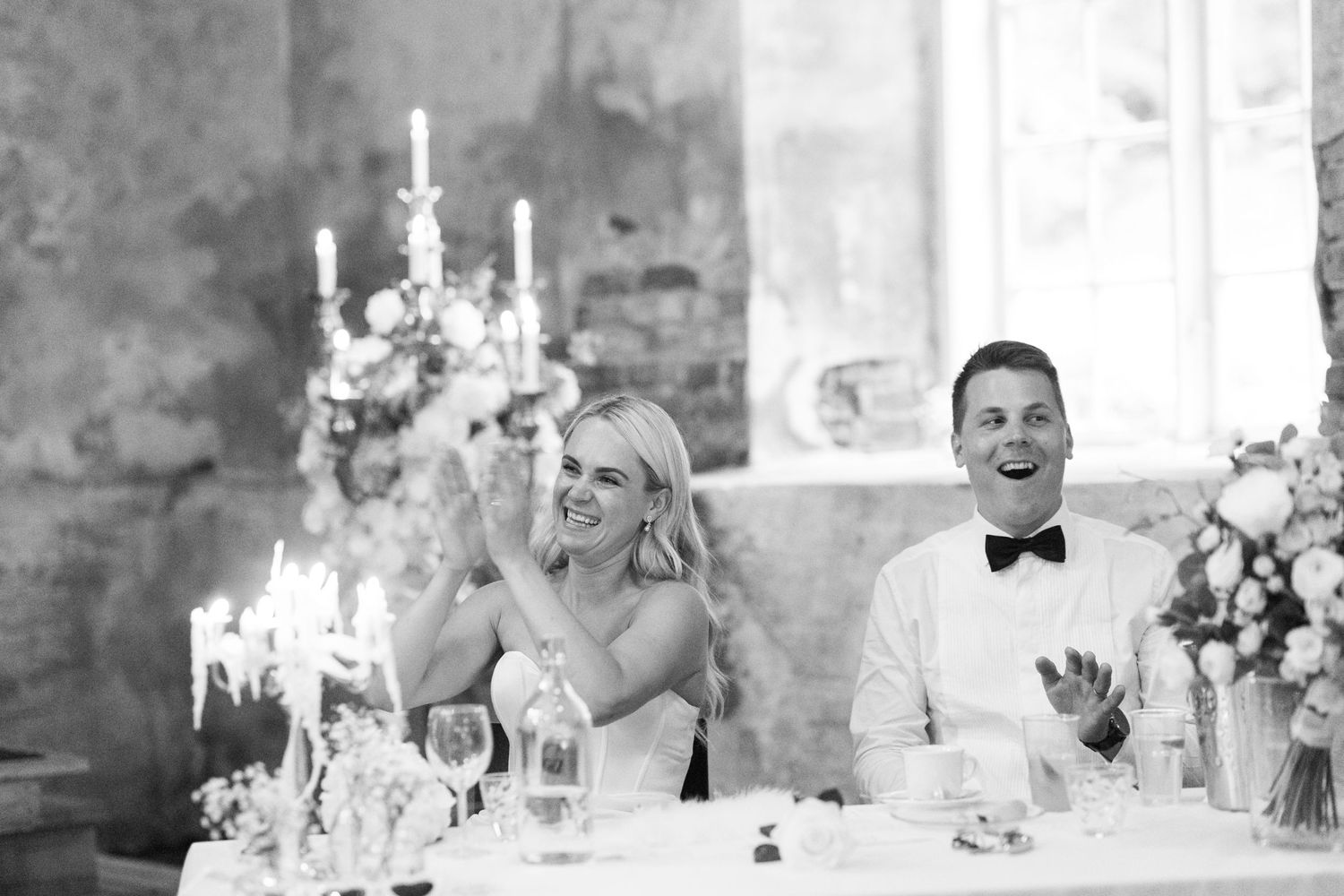 Black and white photo of a couple laughing during their wedding reception.