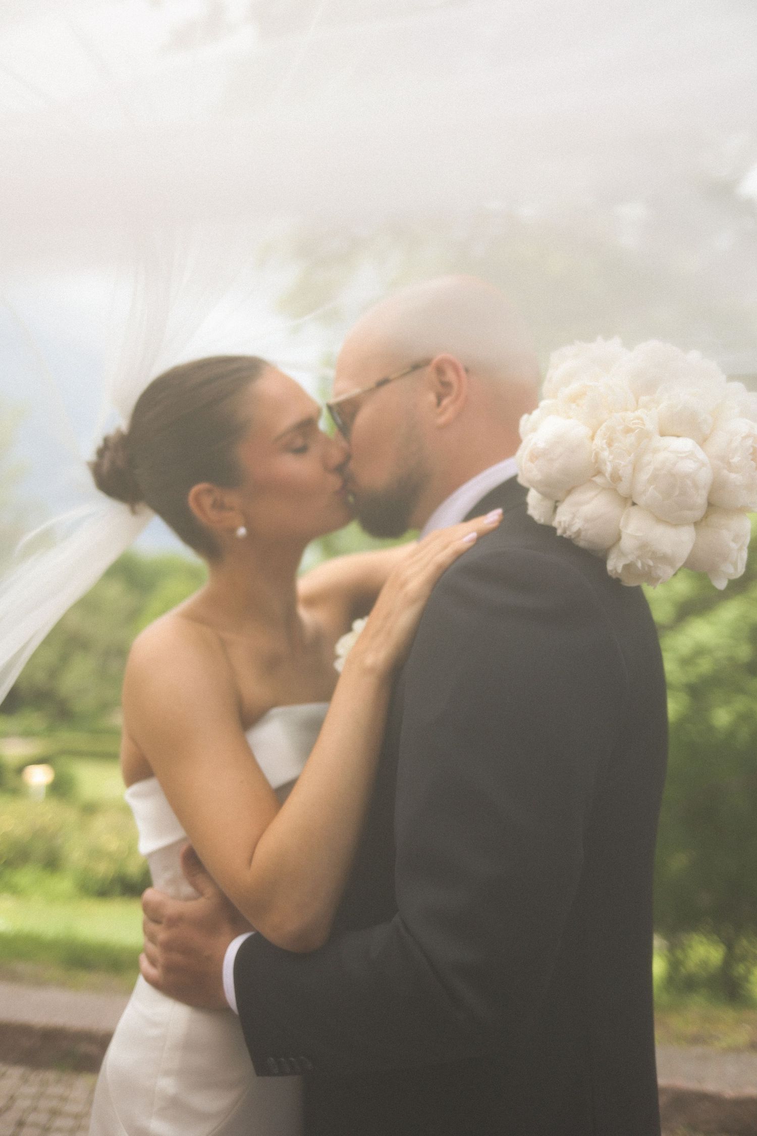 A romantic wedding kiss captured in soft, dreamy light outdoors.