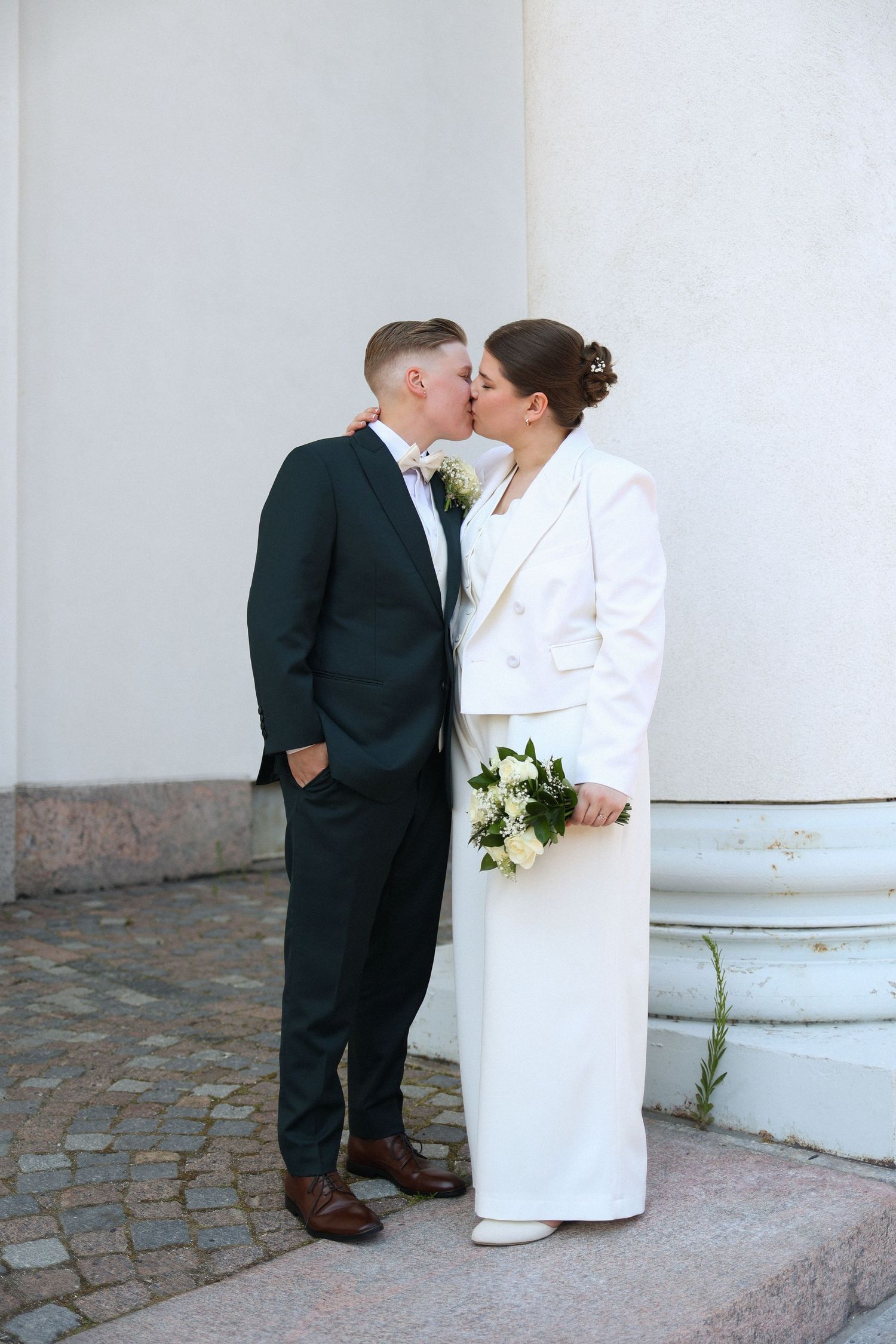 Classic wedding portrait of couple in white and black attire against white wall.