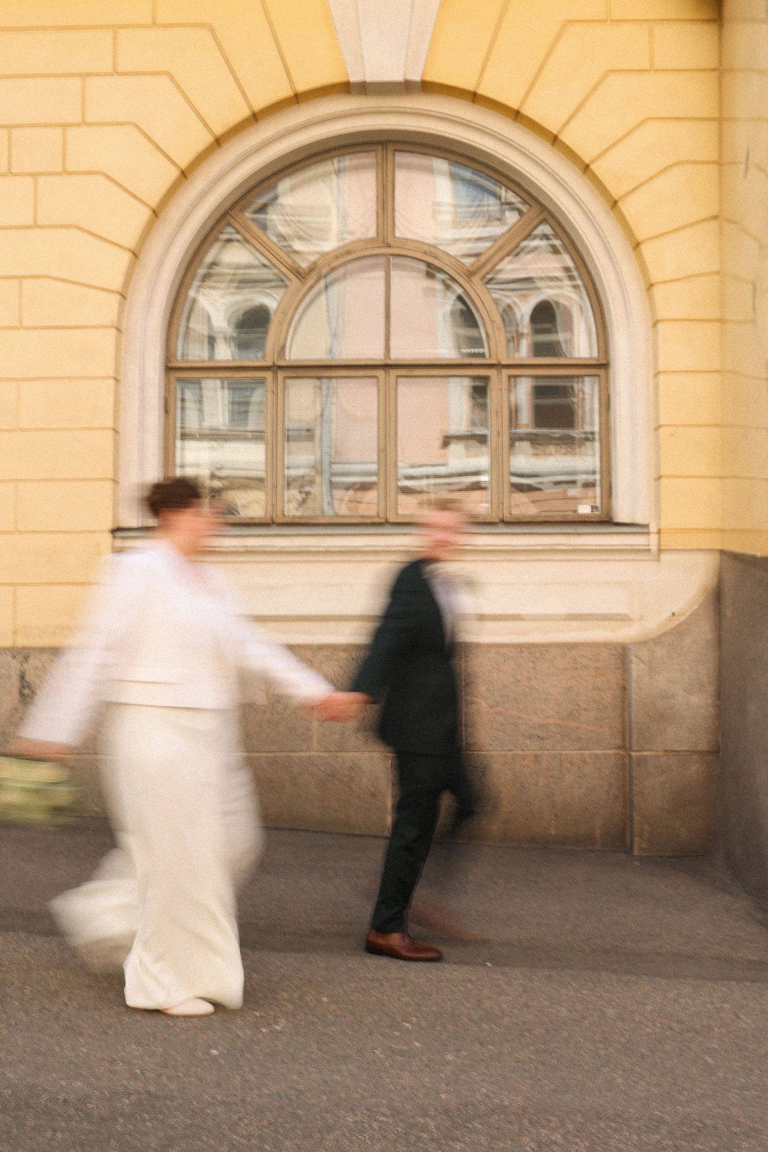 Motion-blurred candid shot of couple walking past arched window on wedding day.
