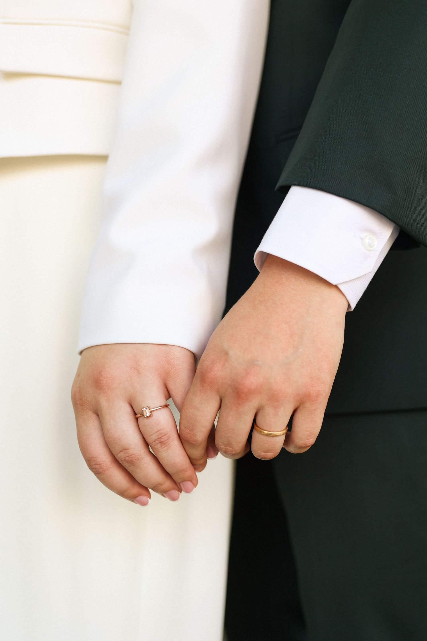 Close-up of couple's hands with wedding rings against black and white attire.