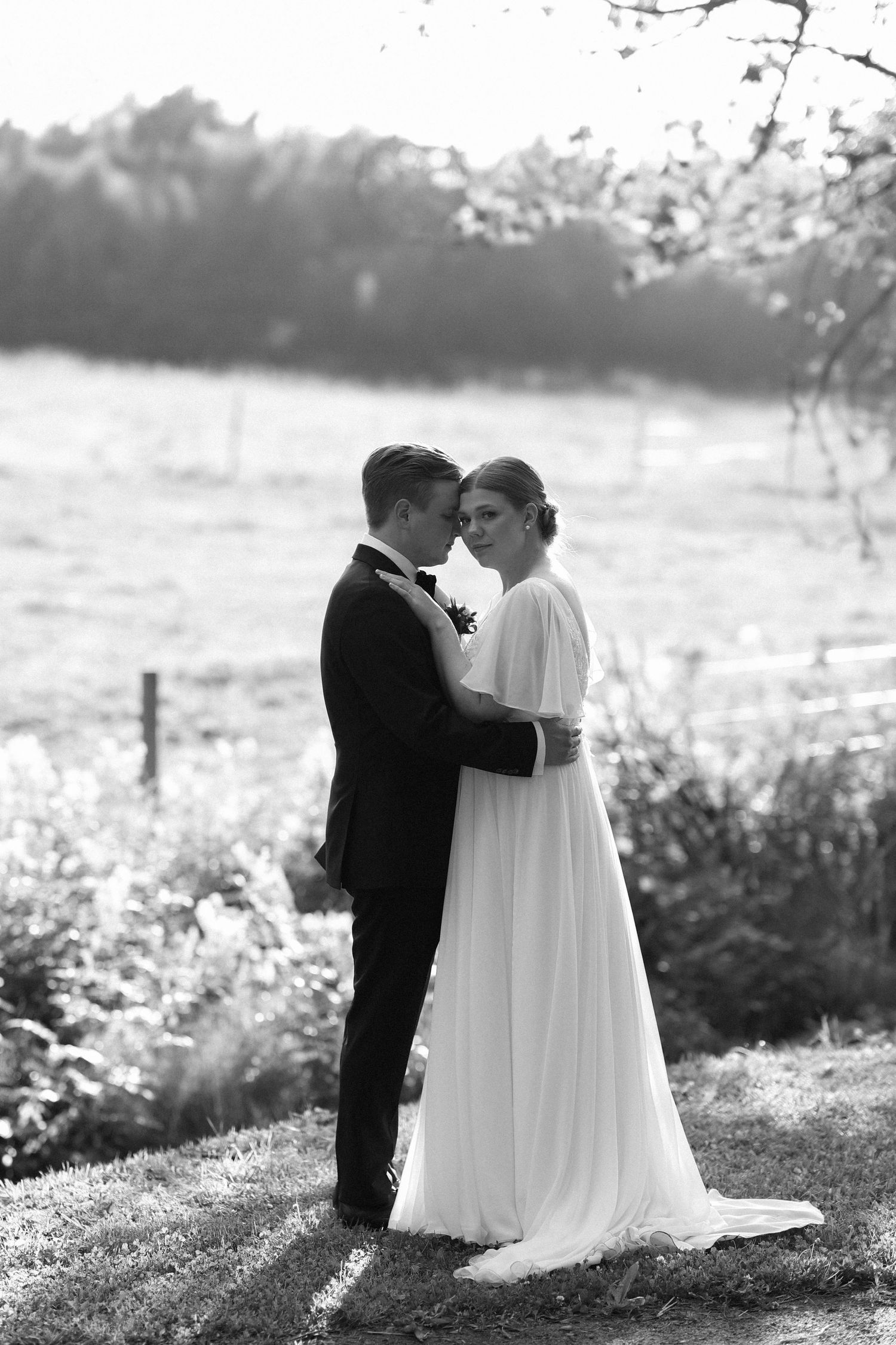 Black and white portrait of a couple in wedding attire standing close together in a garden setting.