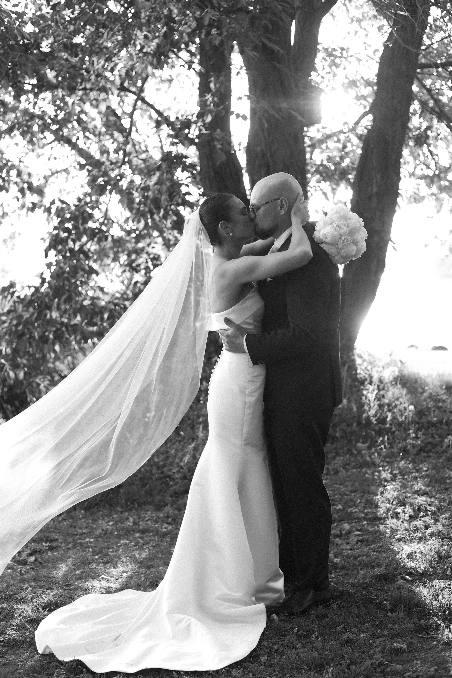 Dramatic black and white wedding photo showing couple in intimate embrace with flowing veil.