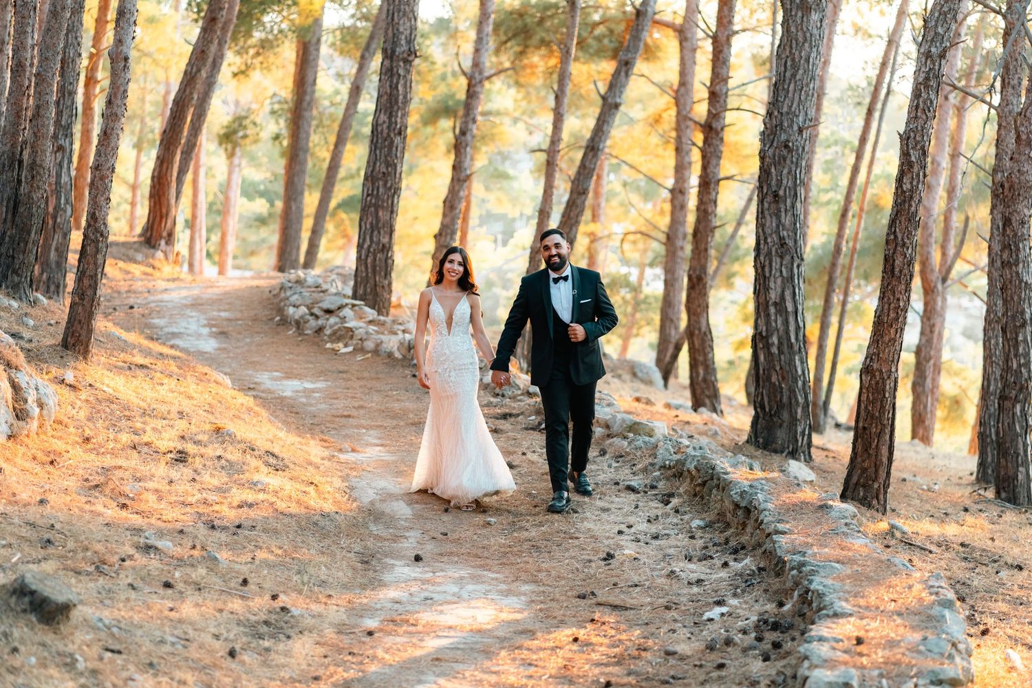 Wedding couple walking along pine forest trail in golden afternoon light.