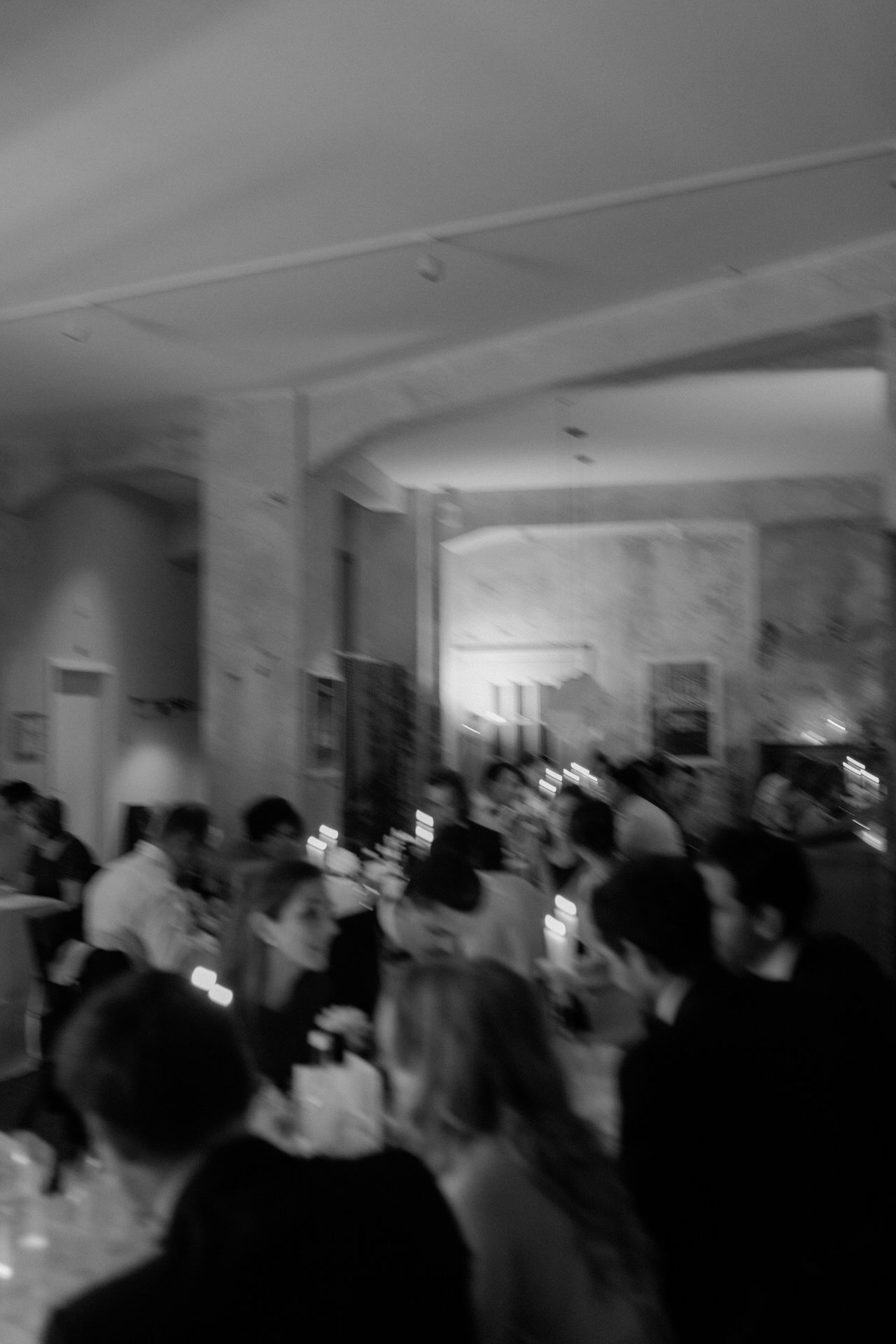 Blurred black and white image of a wedding dress with an off-shoulder neckline and flowing fabric.