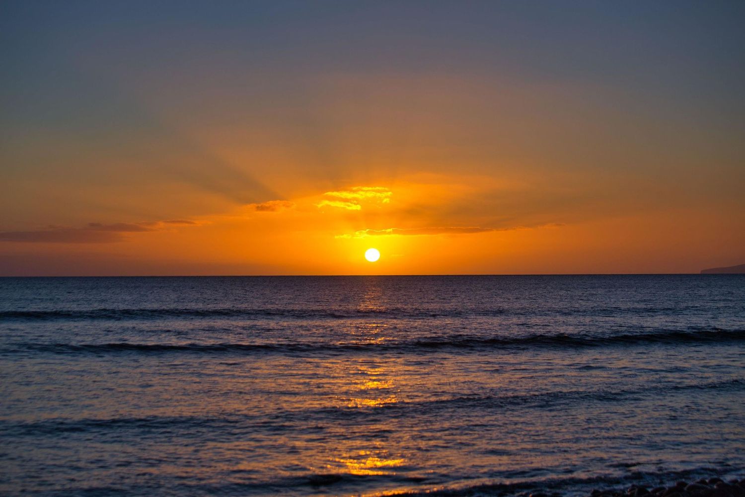 Vibrant orange sunset over calm ocean waves with glowing sun on horizon.