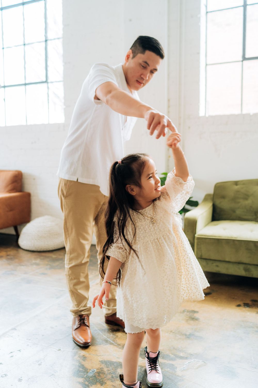 A parent and child in casual attire dance together in a bright modern living room with a green sofa.